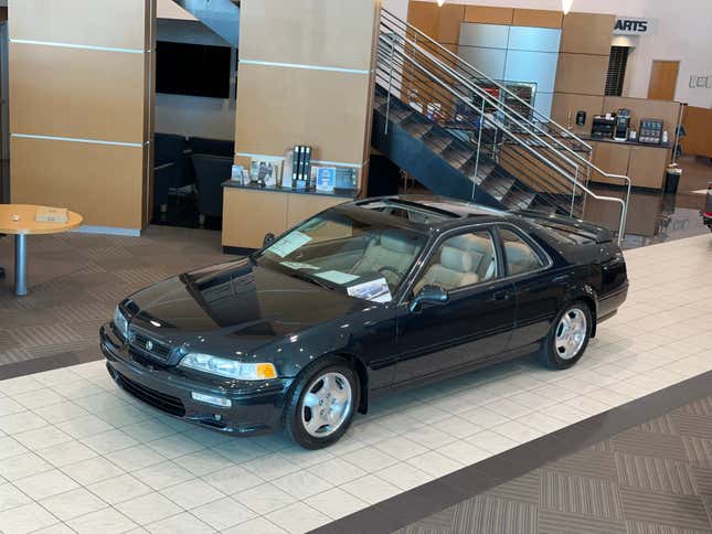 A sherwood green 1995 Acura Legend LS Coupe is on display in a very beige car dealership showroom.