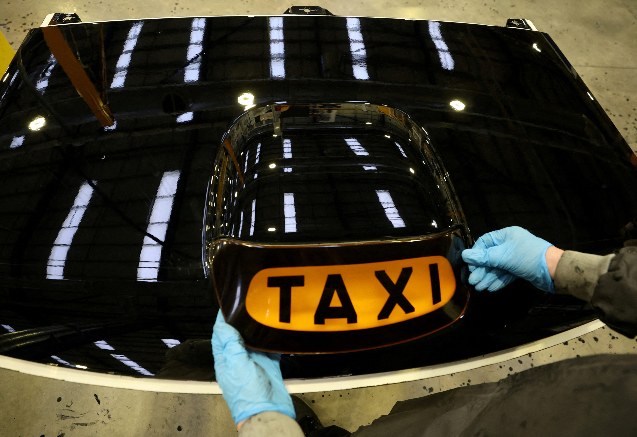 A worker places a taxi sign onto the roof panel of a TX electric taxi inside the LEVC (London Electric Vehicle Company) factory in Coventry