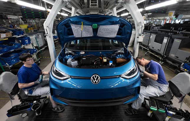Volkswagen production line showing the finishing touches being put on a blue VW ID.3. Two men sitting on either side of the car working on it.